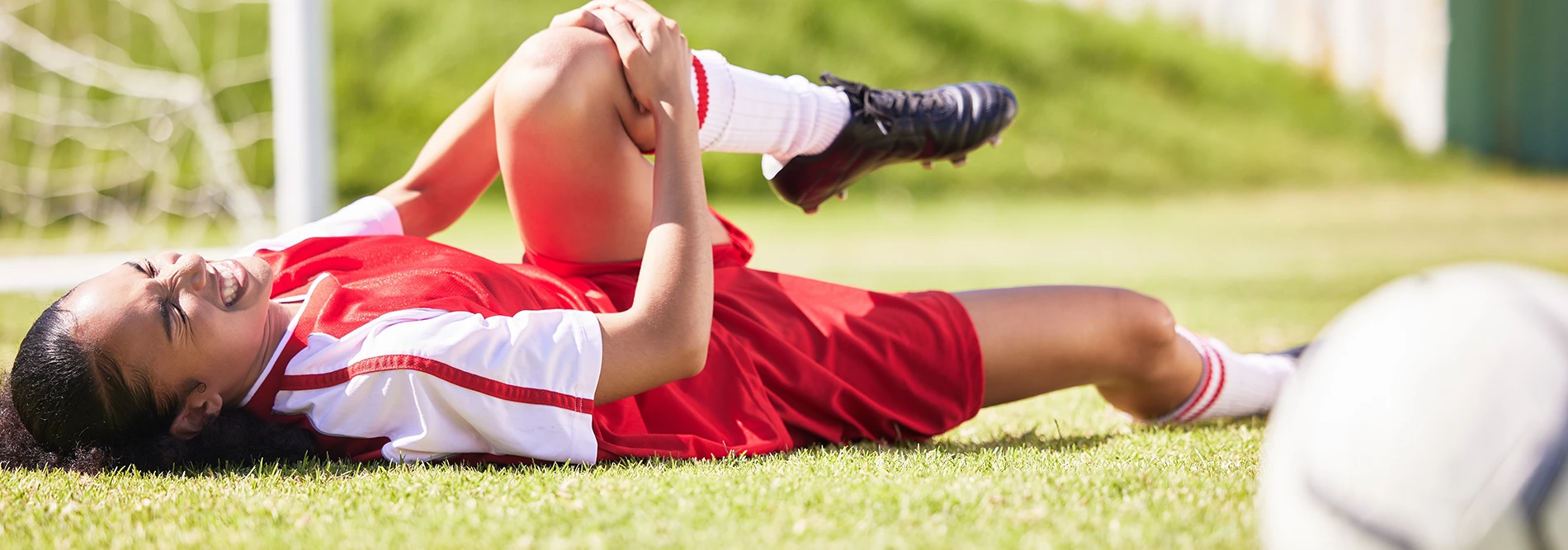 soccer player holding knee while lying on the ground appearing to be in pain
